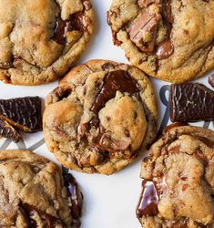 several chocolate chip cookies on a white plate with candy bars in the middle and one cookie half eaten