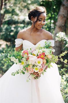 a woman in a wedding dress holding a bouquet and smiling at the camera with trees behind her