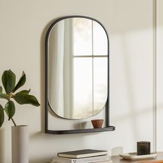 a mirror is hanging on the wall above a table with books and a plant next to it