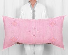 a man holding a pink decorative pillow in front of his face and white shirt behind him