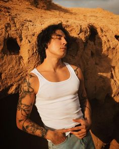 a man with tattoos leaning against a rock