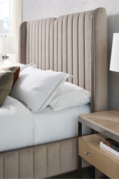 a bed with white sheets and pillows in a bedroom next to a lamp on a nightstand