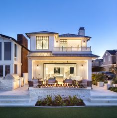 a large white house with lots of windows and lights on the front porch, surrounded by grass