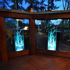 two glass windows with plants on them in front of a wooden deck at night time