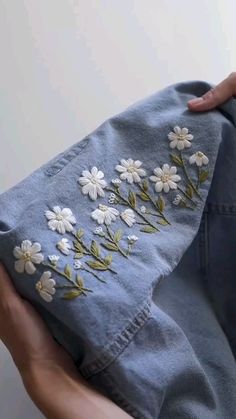 someone is holding an old pair of jeans with embroidered flowers on them