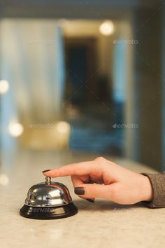 a woman's hand is holding the top of a bell on a counter in a hotel lobby