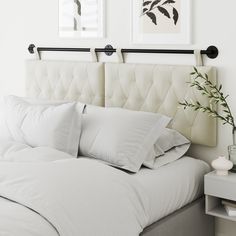 a bed with white linens and pillows in a small room next to two pictures on the wall