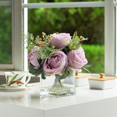 a vase filled with pink flowers sitting on top of a table next to a cup and saucer