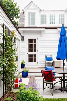 an outdoor patio with chairs, table and umbrellas in front of a white house