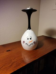 a white vase sitting on top of a wooden table next to a wall with a face painted on it