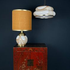 a lamp sitting on top of a red cabinet next to a light fixture with a gold shade