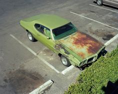 an old rusty green car parked in a parking lot next to a silver truck with rust on it's hood