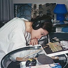 a woman wearing headphones is sleeping on a table with books and other items in front of her