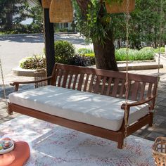 a wooden swing with cushions on it in front of a tree and some potted plants