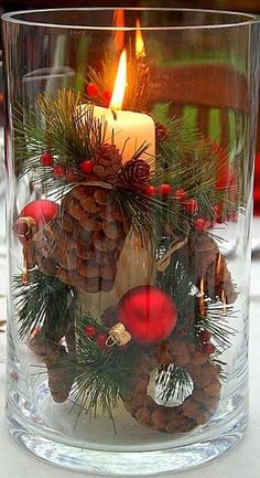 a candle that is sitting inside of a glass vase with pine cones and ornaments on it