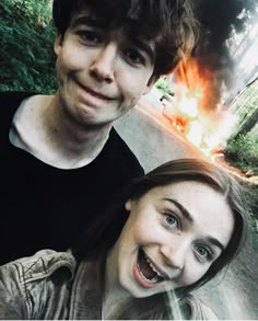 two people standing next to each other in front of a fire