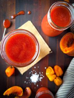 two jars filled with red liquid sitting on top of a table next to sliced peaches