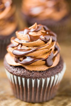 two chocolate cupcakes with frosting on top sitting on a wooden table next to each other