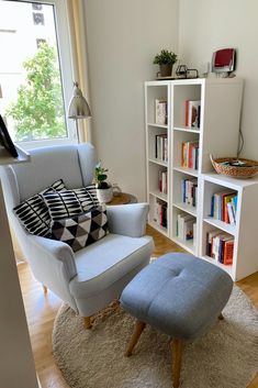 a living room with a chair, ottoman and bookshelf