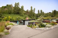 a house with lots of plants and flowers in the front yard on a hill side