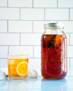 a mason jar filled with liquid next to a glass full of ice and orange slices