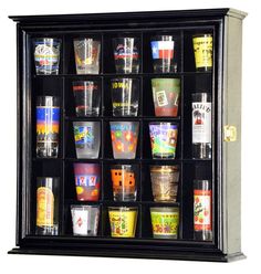 a display case filled with lots of different types of shot glasses on top of a white wall