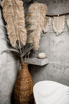 a vase filled with dry grass next to a white bowl and wall hanging on the side