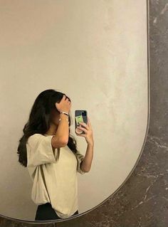 a woman taking a selfie in front of a mirror with her cell phone up to her ear