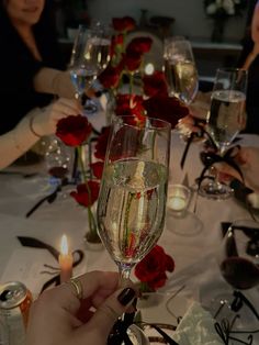 a person holding a wine glass in front of some glasses on a table with roses and candles