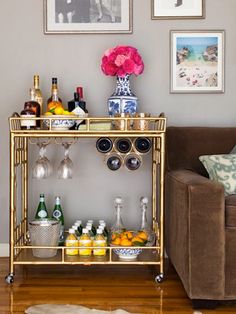 a gold bar cart with bottles and glasses on it in front of a brown couch