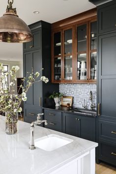 a kitchen with black cabinets and marble counter tops, white sink and gold faucet