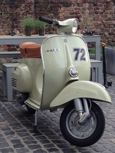 an old scooter is parked in front of a brick wall and table with potted plants