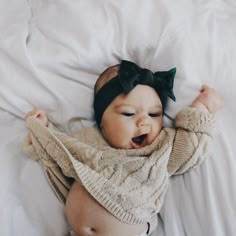 a baby with a bow laying on top of a bed wearing a sweater and pants