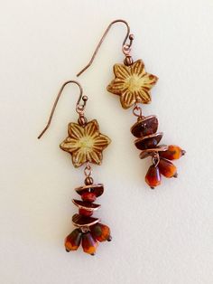 "Perfect for Autumn! Orange, straw, and and copper flower earrings featuring 16 mm carved straw colored Picasso flower wire wrapped with dangling orange Picasso teardrops and hammered copper discs. Tiny 6x8 mm burnt orange teardrops have lovely brown and blue Picasso finish on the ends and are separated by wavy copper discs and translucent fire orange Czech glass beads for extra sparkle. Earrings hang from antique copper French ear hooks and measure 2 1/4\" long." Cinnamon Colored Earrings, Orange Accessories Aesthetic, Nature-inspired Brown Flower-shaped Jewelry, Adjustable Copper Flower Earrings, Bohemian Brown Flower Earrings, Brown Dangle Flower Earrings, Handmade Copper Flower Earrings, Brown Dangle Flower Earrings For Pierced Ears, Brown Flower Earrings With Ear Wire