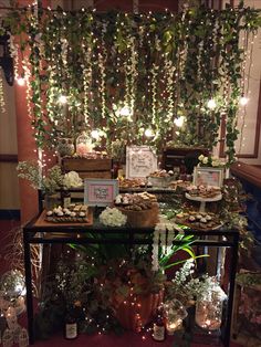 a table topped with lots of food and greenery next to a wall covered in lights