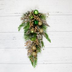 a green and gold christmas ornament hanging on a white wooden wall with pine cones