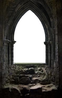 an arched window in the side of a stone building with rocks and grass on the ground