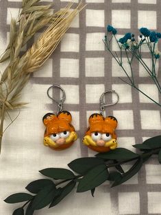 two orange and yellow tiger shaped key chains sitting on top of a piece of cloth