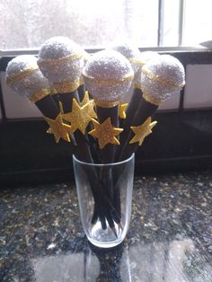 five gold stars in a clear glass vase on a countertop next to a window