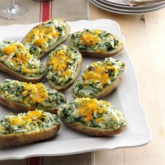 baked potatoes with cheese and spinach are on a white plate next to wine glasses