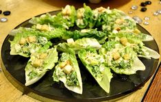 a black plate topped with lettuce and croutons on top of a wooden table