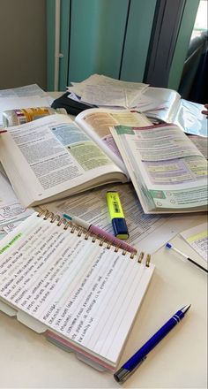 several open books on a table with pens and pencils in front of one book