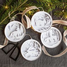 four white christmas ornaments hanging from a pine tree with scissors and measuring tape on the table