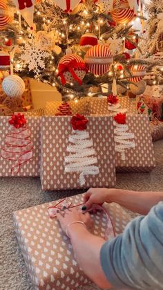 a woman is wrapping presents under the christmas tree