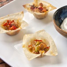 small tortilla cups with salsa and sour cream on a white plate next to a bowl