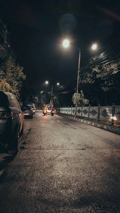 cars are parked on the side of an empty street at night with lights above them