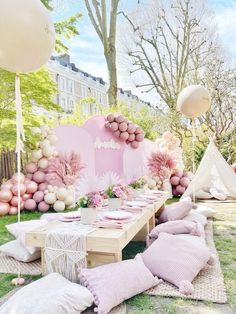 an outdoor party setting with pink and white balloons, pillows, and decorations on the grass