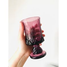 a hand holding a purple glass cup in front of a white wall