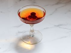 a close up of a drink in a wine glass on a marble counter top with light coming from behind it