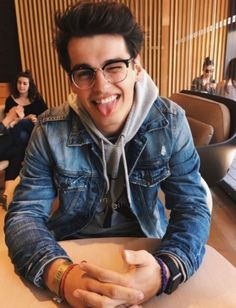 a young man sitting at a table with his tongue out and people in the background